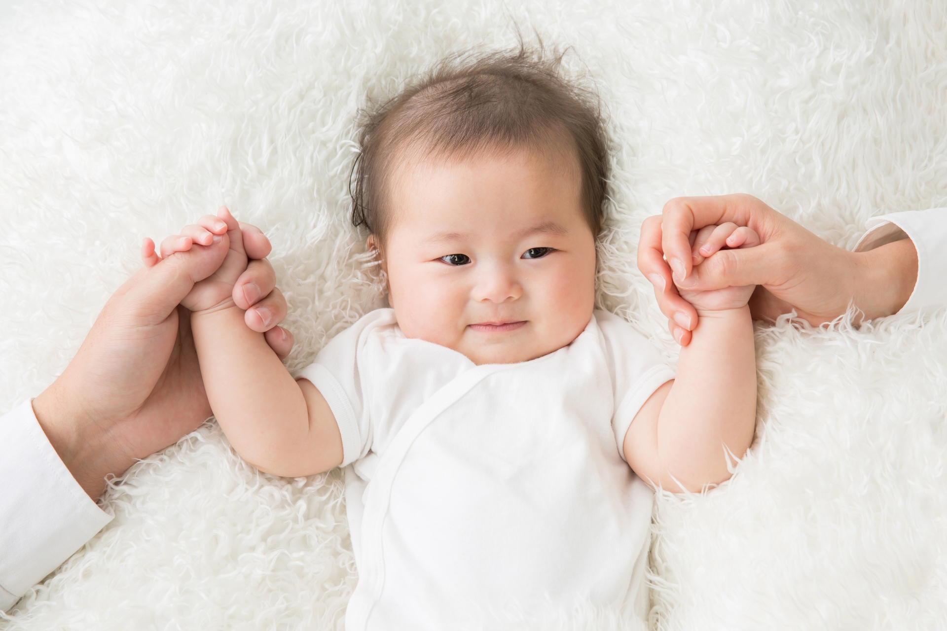 両親に手を握られる赤ちゃん